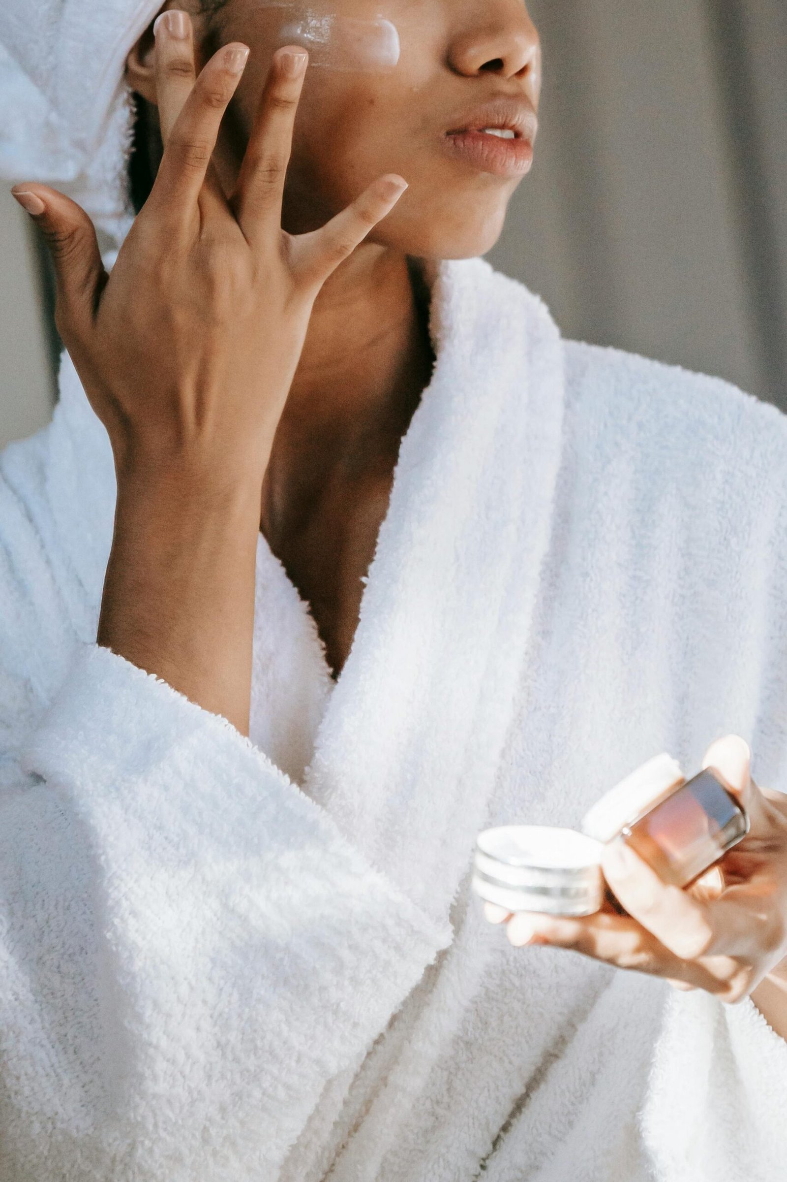 Self esteem young African American lady with moisturizing sheet mask and towel on hand wearing trendy sunglasses while standing against blue background in bathrobe after shower